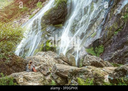Woman sitting on rocks looking at Powerscourt Waterfall in County Wicklow Ireland scenic nature landscape. Stock Photo