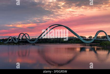 Sunrise over the pedestrian bridge across the Dnipro River in Kyiv, Ukraine. Golden sunlight breaks through pink clouds, reflects on calm water Stock Photo