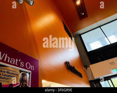 Liverpool, UK - May 16, 2026: Bright museum lobby interior in Liverpool, UK with orange wall, signage, poster and large windows. Stock Photo