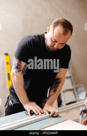 Builder preparing aluminum profiles for stretch ceiling using special equipment in apartment being renovated Stock Photo