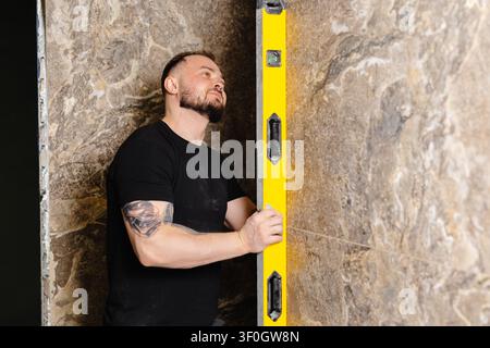 Builder checking the evenness of marble tiles with a level tool, ensuring precision and accuracy during renovation work on a wall Stock Photo