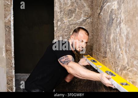 Builder checking the evenness of marble tiles with a level tool, ensuring precision and accuracy during renovation work on a wall Stock Photo