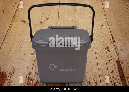 Small grey indoor plastic caddy with lockable lid against a wood background for domestic food waste that is collected and recycled Stock Photo