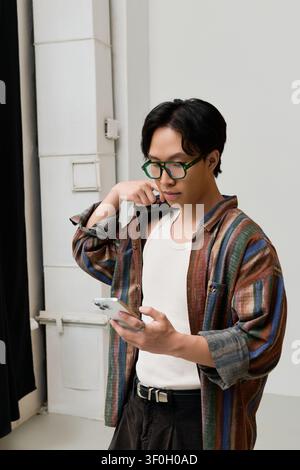 A handsome young man dressed elegantly checks his smartphone while posing in a contemporary setting. Stock Photo