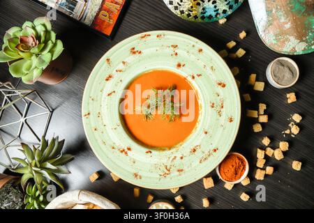 A bowl of soup is placed on a table alongside a stack of crackers and succulents. Stock Photo