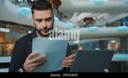 Serious focused Caucasian man businessman working with laptop and documents managing finance budget in business center male guy employer agent work Stock Photo