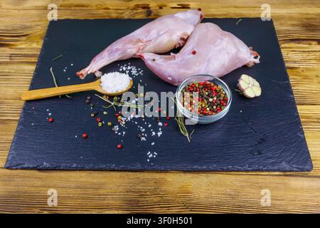 Raw rabbit legs with spices on a black slate cutting board on wooden table Stock Photo