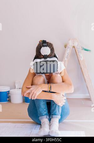 Woman in virtual reality headset visualizing home renovation while sitting on floor with blueprints Stock Photo