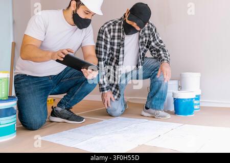 Construction workers collaborating on renovation plans, checking blueprints and a digital tablet for project details Stock Photo