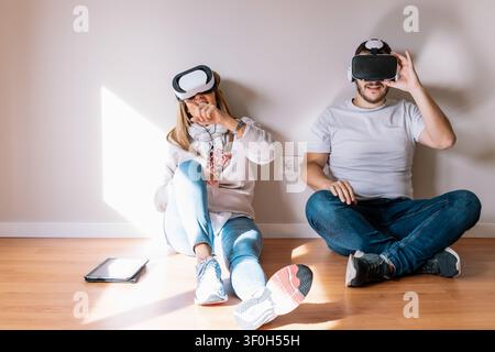 Young couple enjoying virtual reality technology together while sitting on the floor Stock Photo