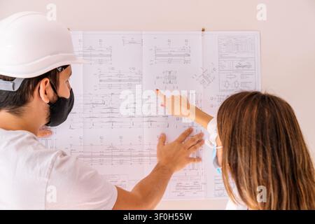 Two engineers discussing building plans and pointing at a large blueprint on the wall Stock Photo