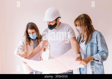 Three people wearing face masks discussing construction plans for a house project Stock Photo