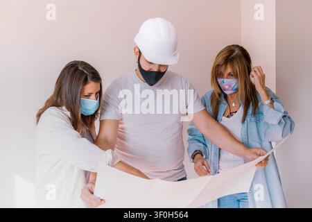 Group of people in face masks discussing building plan for new house project Stock Photo
