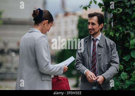 Business colleagues exchanging documents and smiling during an informal outdoor meeting on a city sidewalk Stock Photo