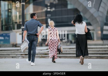 Three colleagues walking together in a modern urban plaza carrying bags and folders Stock Photo