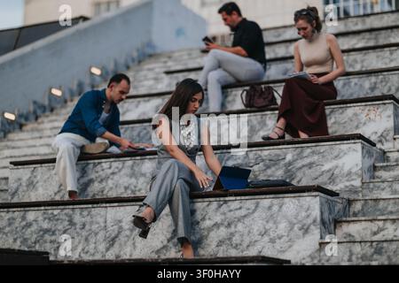 Business professionals working outdoors on marble steps with laptops and tablets in corporate collaboration Stock Photo