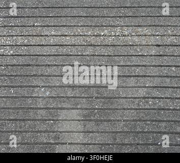 Horizontal close up of a cement walk ramp surface with grooves, rough mixed‑pebble texture, scattered debris, and light weathering Stock Photo