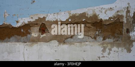 Horizontal close up of a weatherworn deteriorating painted wall surface with cracked peeling paint, broken concrete layers Stock Photo