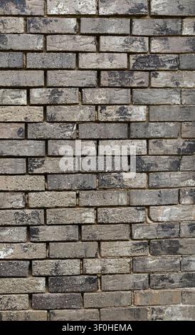 Vertical close up of a light brown brick wall surface with worn mortar, showing weatherworn bricks with white and black pebbles Stock Photo