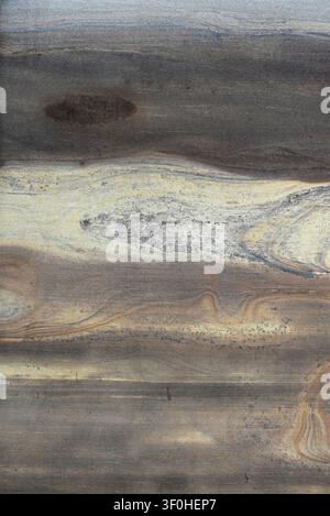 Vertical close up of a sandstone slab with multiple color bands, flowing ribbons with mineral streaks, an oval feature in the upper band Stock Photo