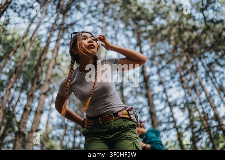 Young woman hiking in a pine forest looking up while exploring outdoors on a trail Stock Photo