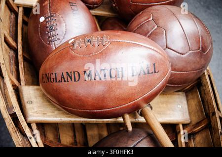 A close-up shot of an antique rugby ball made of shiny brown leather. The textured surface features the black stamped inscription England Match Ball a Stock Photo