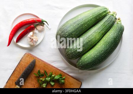 Fresh round zucchini with dark green skin and light spots on white background with red pepper and garlic, mint leaves. Natural vegetables for cooking Stock Photo