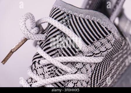 Close-up sneaker lace detail with woven fabric pattern, showcasing intricate material texture, light gray laces, subtle black accents, clean modern de Stock Photo