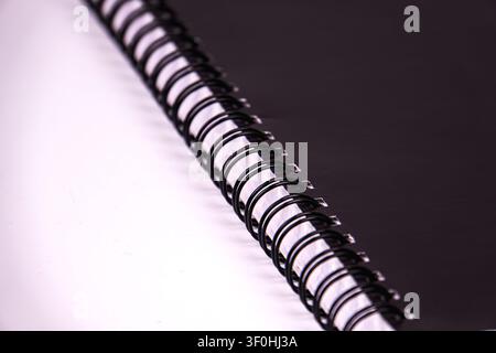 Black spiral notebook binding close-up focus, showcasing metallic sheen, reflective surface, clean gradient background, sharp details, modern sleek ap Stock Photo