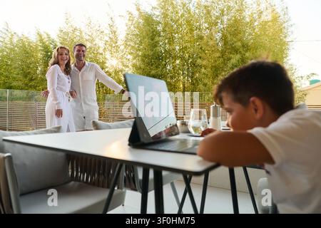 Happy Family on Home Balcony Terrace With Child Using Laptop and Parents Enjoying Sea View Stock Photo
