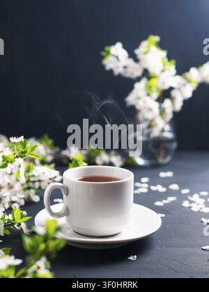 Blooming cherry branches and a mug of fragrant green herbal tea. Spring composition Stock Photo