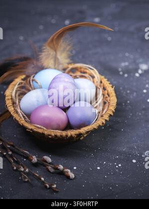 Pastel-colored Easter eggs in a wicker basket on a dark table, willow branches Stock Photo