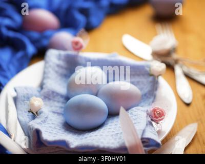 Naturally colored stylish Easter eggs in a plate, decorative flowers, on a wooden table Stock Photo
