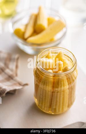 Bright close-up of pickled baby corn packed in a glass jar with brine, ideal for pantry, cooking, recipes, and rustic food styling. Warm yellow tones Stock Photo