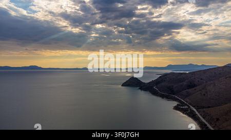 Evocative aerial shot capturing the sunset over the coastline of Sagiada, Greece. Crepuscular rays filter through dark clouds, illuminating the Ionian Stock Photo