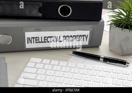 Intellectual Property label on folder, computer keyboard and pen on wooden table, closeup Stock Photo