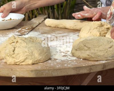 Hands preparing traditional Cretan bread dough on a rustic wooden table scattered with flour during an authentic outdoor baking workshop. Stock Photo