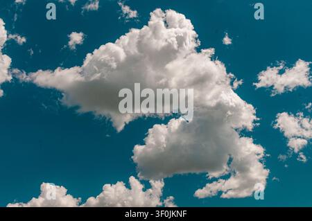 Large, puffy white cumulus clouds floating in a bright blue sky on a sunny day. The scene is peaceful and bright, perfect for a summer background. Stock Photo