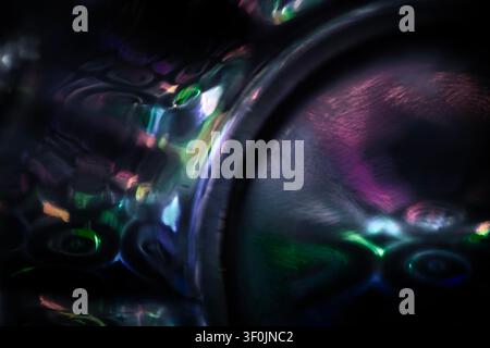 Abstract close-up of iridescent reflections on dark glass, with neon green, purple and blue light patterns creating a surreal textured surface. Stock Photo