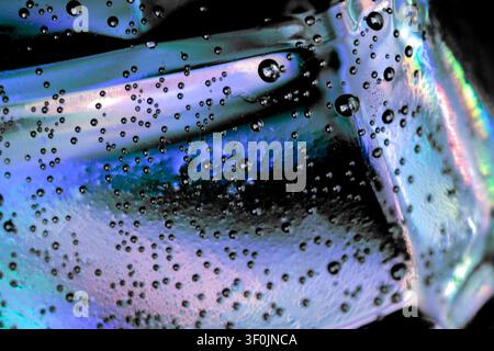 Macro abstract of tiny air bubbles trapped in iridescent glass, with blue, aqua, black and rainbow light refractions creating a futuristic texture. Stock Photo