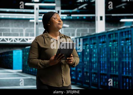 Data center technician uses a tablet to monitor performance metrics and review server capacity, supporting reliable infrastructure operations. Stock Photo