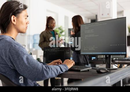 Focused software developer typing at desktop pc in office. Programmer diligently works on web development tasks, demonstrating concentration and commitment to completing coding projects efficiently. Stock Photo