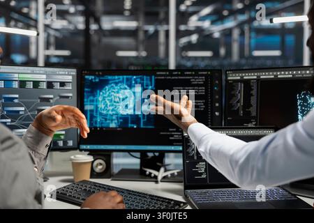 Server room technicians planning solutions, collaborating in office, working with AI computerized model. Stock Photo