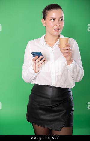 Woman drinking a hot drink while scrolling social networks on a green background Stock Photo