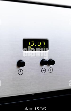 Close-up of a stainless steel oven control panel featuring a green digital clock reading 12:47 and black knobs with plus and minus buttons in a modern Stock Photo