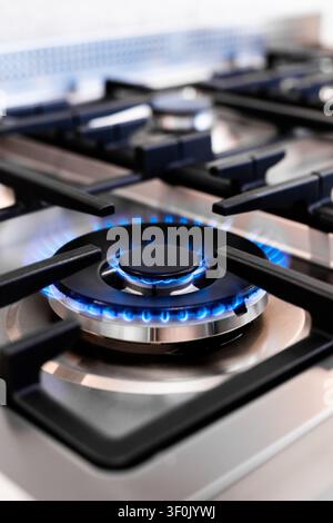 Detailed close-up of a modern gas stove burner with bright blue flame, stainless steel surface and cast iron grates, showing home kitchen cooking ener Stock Photo
