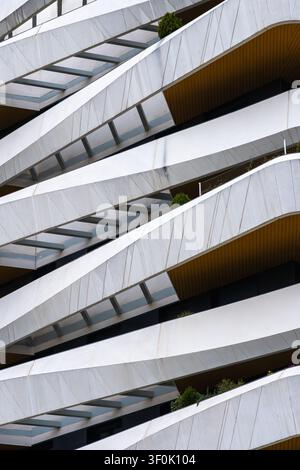 Abstract view of a contemporary building facade with sweeping curved balconies, repeating diagonal lines, metal cladding, and small greenery accents, Stock Photo