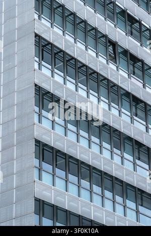 Close-up of a modern office building facade with repeating grid windows, reflective glass, and textured metal panels, creating an abstract architectur Stock Photo
