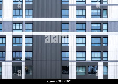 Close-up of a contemporary apartment building facade with repeating windows and black, white, and gray panels, creating a clean geometric pattern and Stock Photo