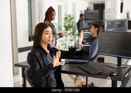 Asian female programmer works with 3d interface in office, testing code for web development. Woman developer with arms raised, interacting with holographic screen and analyzing frontend data. Stock Photo